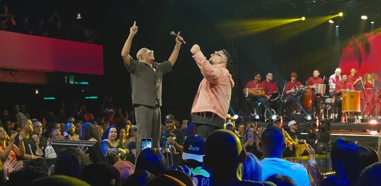 Pezinho e um convidado de braços erguidos no palco, com a banda ao fundo e a plateia em primeiro plano