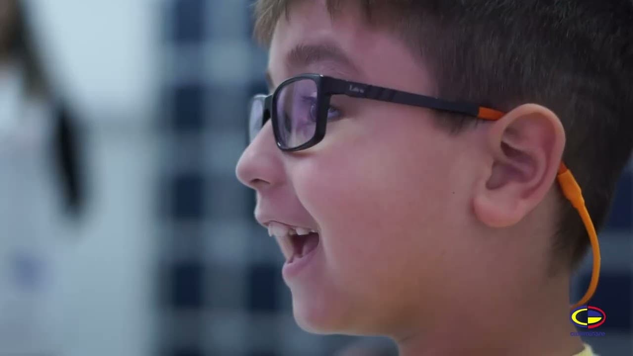 Menino de óculos sorrindo de perfil, em um ambiente interno